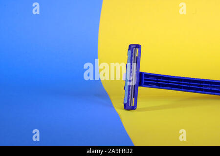 Blue shaving blade on yellow and blue background. Disposable razor for men. Stock Photo
