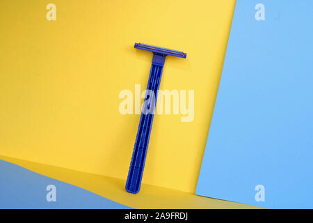 Blue shaving blade on yellow and blue background. Disposable razor for men. Stock Photo