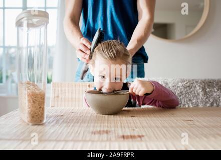 father brushing his daughters hair at breakfast before school Stock Photo