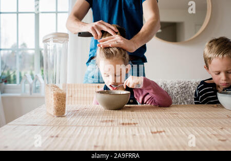 father brushing his daughters hair whilst eating breakfast Stock Photo