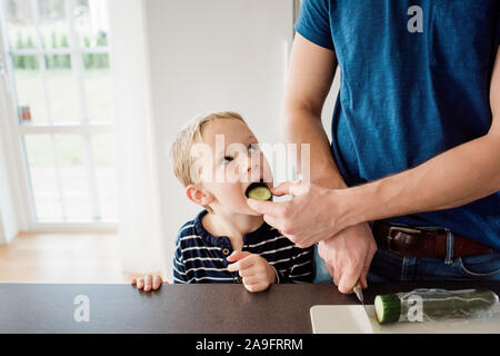 father making his kids packed lunch whilst feeding his son for school Stock Photo