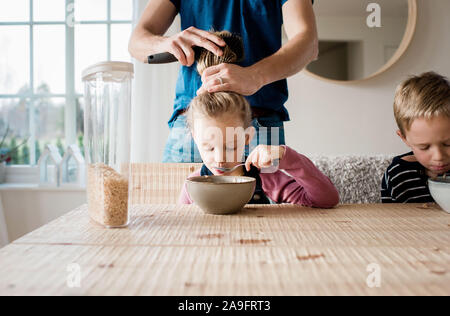 father brushing his daughters hair at breakfast table before school Stock Photo