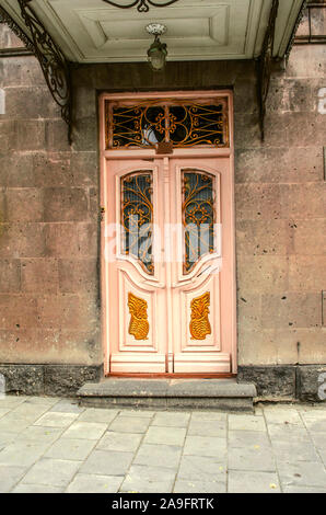 Old milky pink double doors with Windows covered with wrought iron bars and figures of Golden color on the facade of a stone house under a canopy in t Stock Photo