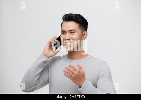 Thoughtful happy asian man smiling while talking on mobile phone isolated against white background Stock Photo