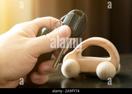Male hand holds car keys next to a small wooden car. Stock Photo