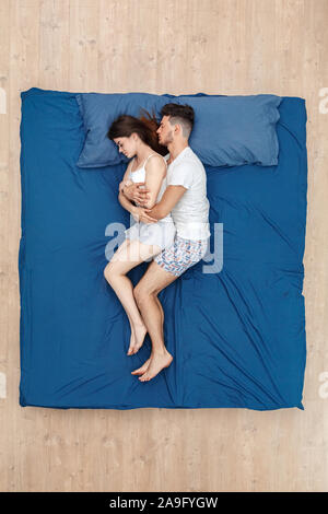 Bedtime. Young couple sleeping together on bed top view hugging Stock Photo