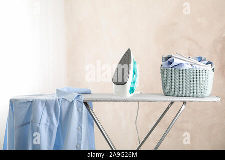 Iron and basket with clear laundry against light background, space for text Stock Photo