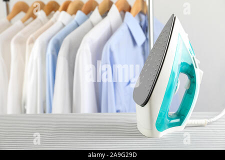 Iron on ironing board against light background, space for text Stock Photo
