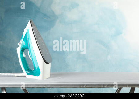Iron on ironing board against blue background, space for text Stock Photo