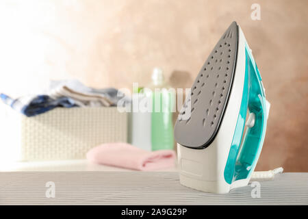 Iron on ironing board against brown background, space for text Stock Photo