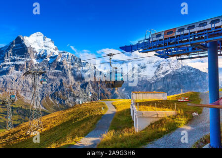 Grindelwald, Switzerland cable car cabins arriving to high station First and autumn Swiss Alps mountains panorama landscape, wooden chalets on green f Stock Photo