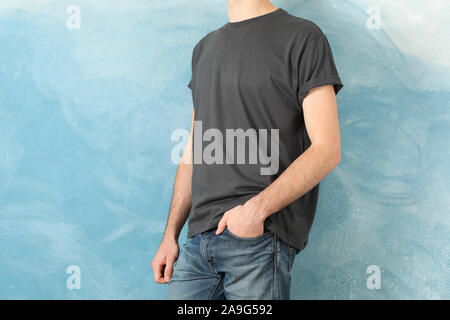 Men in blank grey t-shirt against blue background, space for text Stock Photo