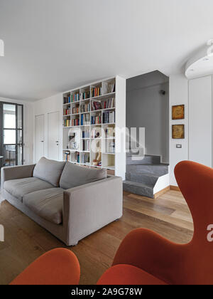 interior shot of a modern living room in foreground the fabric armchair and the fabric sofa behind which there is a white bookcase the masonry stairca