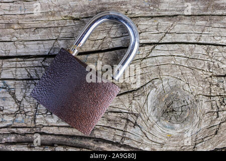 A padlock lies on an old, wooden board with cracks and scratches Stock Photo