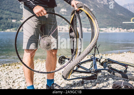 Bike Repair. Man Repairing Mountain Bike. Cyclist man in trouble rear wheel wheel case of accident. Man Fixes Bike near lake in Italy background Stock Photo