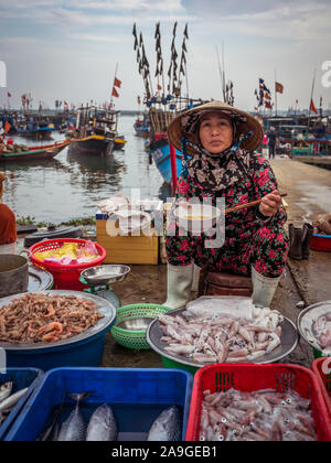Elder Vietnamese female vendor selling fresh fish, seafood and squids at Hoi An main fish market while eating lunch in the morning, Vietnam Stock Photo