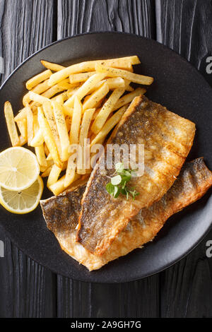 Grilled sea bass fillet with french fries close-up on a plate on the table. Vertical top view from above Stock Photo