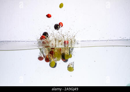 Different fruits and berries falling in water on dark background Stock Photo