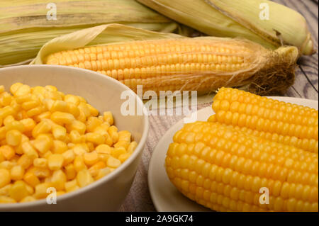 Two boiled ears of corn, corn kernels and untreated ears of corn on a wooden table. Fitness diet. Healthy diet. For a sweet treat. Close up Stock Photo
