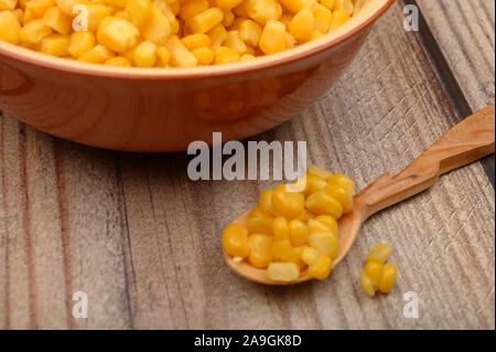 Sweet corn kernels in a plate and on a wooden spoon on a wooden table. Fitness diet. Healthy diet. For a sweet treat. Close up Stock Photo