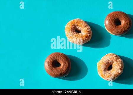 Chocolate frosted donuts and sugar coated donuts on bright blue paper background Stock Photo