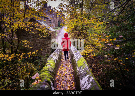 A young women walking towards, across and old stone bridge in the UK countryside on a cold winters day, hiking a local mountain route, Stock Photo