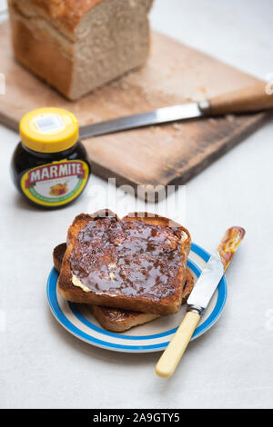Marmite on toast on a plate next to a loaf of white bread and a jar of marmite Stock Photo