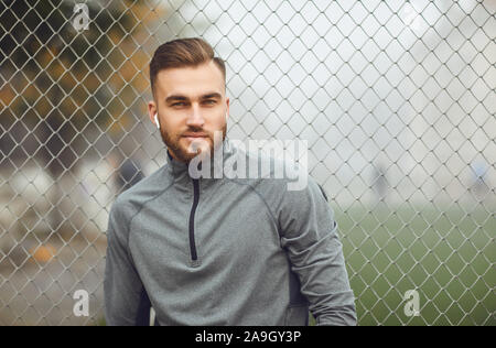 A man bearded man in sports gray clothes is standing against the background of the stadium Stock Photo