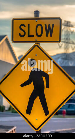 Vertical Pedestrian crossing road sign against houses vehicles mountain and cloudy sky Stock Photo