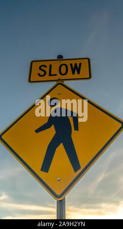 Vertical Yellow Slow sign and pedestrian crossing sign against cloudy sky at sunset Stock Photo