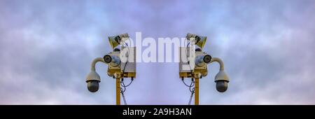 Back to back security cameras with light clouds and sky behind for copy space Stock Photo