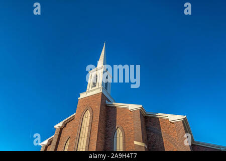 Church with classic red brick exterior wall and white steeple against blue sky Stock Photo