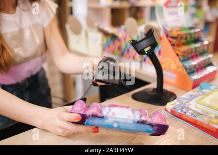Young caucasian female woman cashier in toy store. Woman use cashier counter in kids mall. Stock Photo