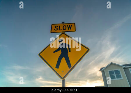 Yellow Slow sign and pedestrian crossing sign against cloudy sky at sunset Stock Photo
