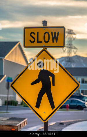 Pedestrian crossing road sign against houses vehicles mountain and cloudy sky Stock Photo