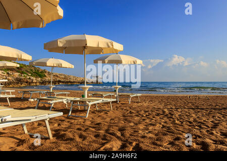 Umbrella beach. The most beautiful beaches of Apulia: Gusmay beach is surrounded by the Mediterranean scrub. In the background a trebuchet. Stock Photo