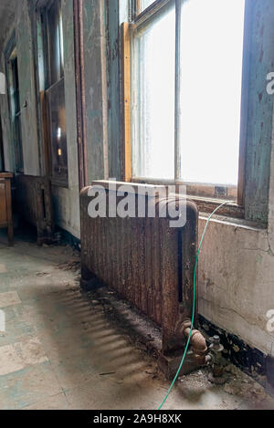 USA, New York, Ellis Island - May 2019: vintage cast iron radiator rusting inside an abandoned hospital ward Stock Photo