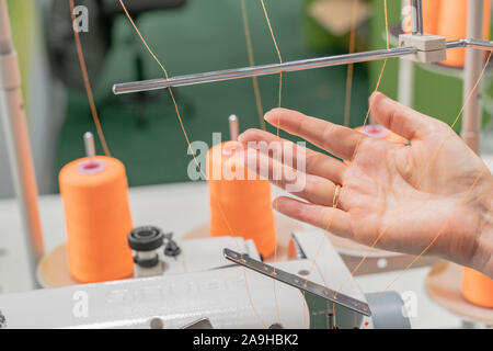 Sewing machine operator sets up a machine. Orange cotton reels are on the background. Horizontal image Stock Photo