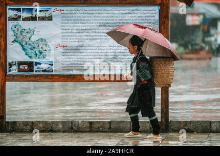 Sapa, Vietnam - 13th October 2019: Local Sapa woman walking through the small mountain town in North Vietnam as she passes the town map board Stock Photo