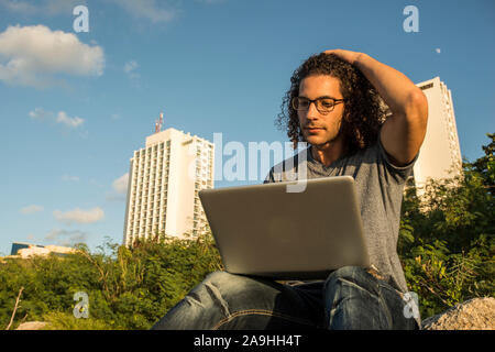 Young Latin man with laptop on the beach Stock Photo