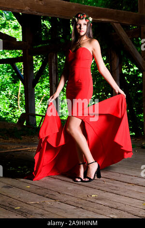 Outdoor high fashion photo of woman in a red evening gown with a floral head piece Stock Photo