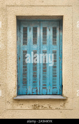 Shutters with wall. Ragged wall with closed shutters on the window. Exterior of old shutters and wall. Background of wall with blue vintage shutters. Stock Photo