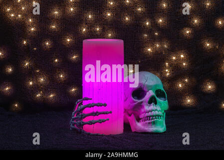 Halloween holiday still life of a pink electric wax candle and a skeleton hand and skull Stock Photo