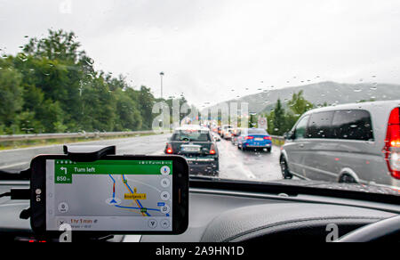 Vehicles queueing  in front of a toll station on a road in Croatia on a rainy day.   A dash mounted mobile phone with a GPS sat nav application indica Stock Photo