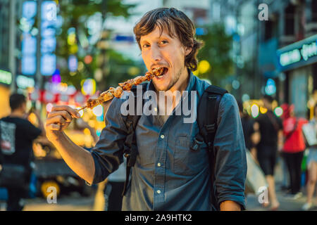 Young man tourist eating Typical Korean street food on a walking street of Seoul. Spicy fast food simply found at local Korean martket, Soul Korea Stock Photo