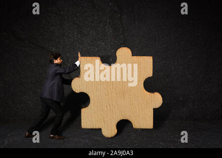 A businessman pushing a piece of puzzle as a business strategy against texture wall Stock Photo