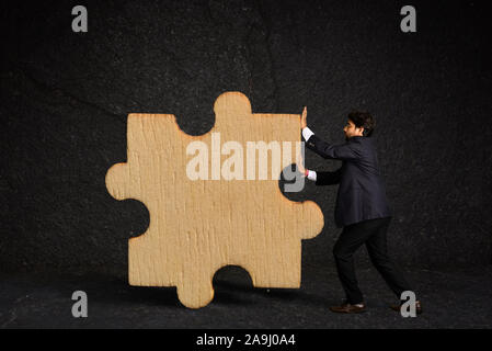 A businessman pushing a piece of puzzle as a business strategy against texture wall Stock Photo