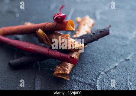 Sweet pureed fruit roll-up pastila. Homemade fruit leather of apple, apricot, strawberry and blueberry on black background. Fruit rolls. Dried fruits. Stock Photo