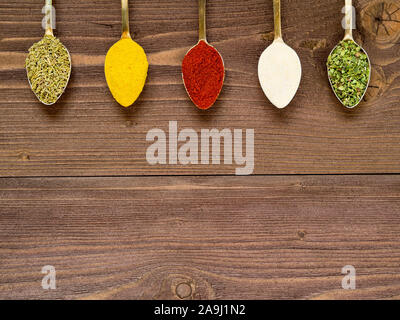 Milled spices - garlic, turmeric, paprika, rosemary, oregano, Golden spoons on a brown wooden table. The view from the top, empty space for text. Stock Photo