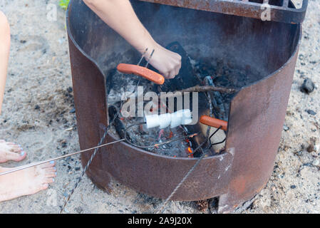 Close-up of marshmallows and hot dogs on roasting sticks cooking over campfire on sandy beach in summer Stock Photo